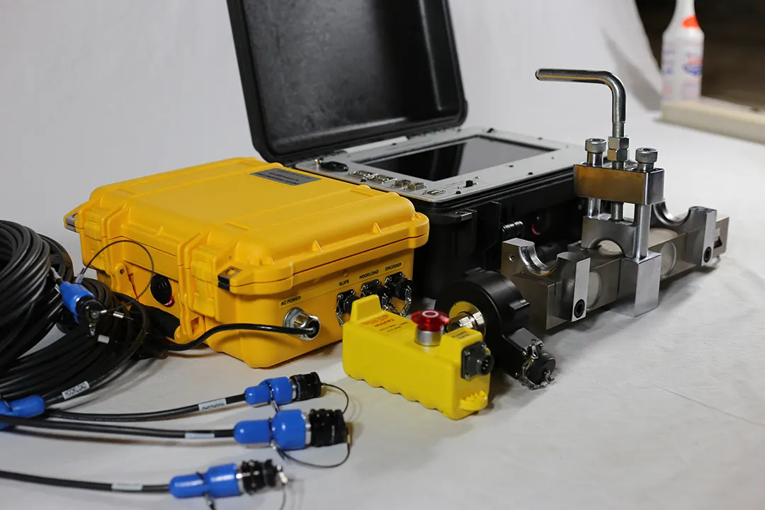 The Depth Tracker kit on a table: the yellow Remote Unit case with AC power, slips, hookload and encoder connectors, a black host case with a built-in touchscreen, the hookload sensor, the drawworks encoder, and sensor cables with blue connectors.